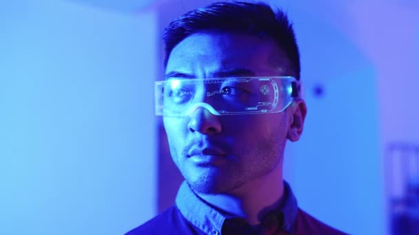 Video al rallentatore di un cinese con occhiali di realtà aumentata che guarda la fotocamera in una stanza blu - Filmati, video