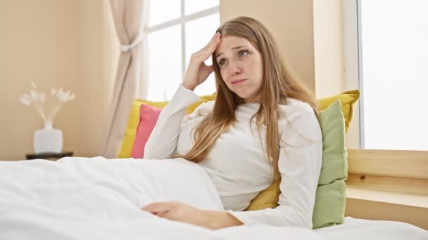 Une jeune femme blonde stressée portant un pyjama s'assoit inquiète sur son lit, aux prises avec une crise imminente dans sa chambre, la main sur la tête indiquant l'énormité du problème. - Séquence, vidéo