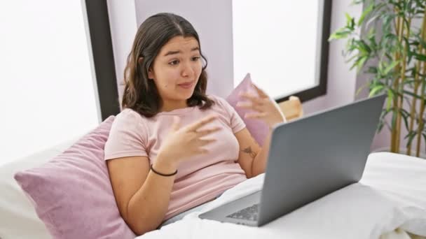 Nuori latino nainen harjoittaa videopuhelu hänen makuuhuone, näyttää karismaa ja mukavuutta sisätiloissa. - Materiaali, video