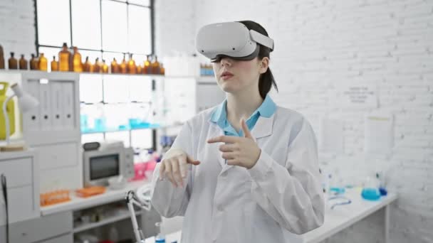 Una joven científica con una bata de laboratorio utiliza gafas de realidad virtual en un entorno de laboratorio moderno - Metraje, vídeo