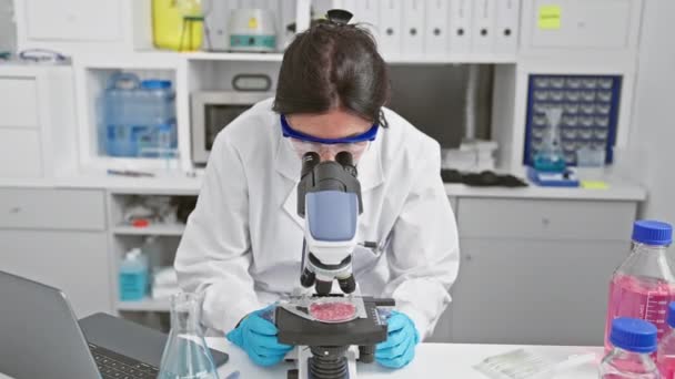 Een lachende vrouwelijke wetenschapper onderzoekt een specimen onder een microscoop in een modern laboratorium, portretteert professionaliteit en expertise in gezondheidsonderzoek. - Video