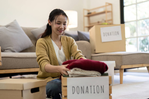 Mujer asiática sosteniendo caja de donación llena de ropa y ropa selecta. Concepto de donación y reciclaje de ropa. Ayudar a los pobres. - Foto, Imagen