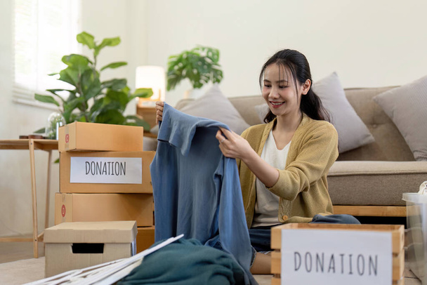 Femme asiatique tenant boîte de don pleine de vêtements et de certains vêtements. Concept de don et de recyclage des vêtements. Aider les pauvres. - Photo, image