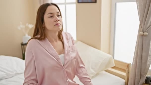 Eine entspannte Frau im rosafarbenen Schlafanzug, die sich in ihrem hellen Schlafzimmer ausbreitet und ein Gefühl von Morgenfrische und Ruhe ausstrahlt. - Filmmaterial, Video