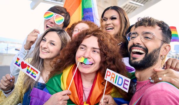 Ομαδική χαρούμενη νεαρούς φίλους που παίρνουν διασκέδαση selfie για τα μέσα κοινωνικής δικτύωσης γιορτάζοντας γκέι ημέρα υπερηφάνειας σε εξωτερικούς χώρους. Διαφορετικοί άνθρωποι που φορούν πολύχρωμα στηρίγματα και σημαίες ουράνιο τόξο. Έννοια της ΛΟΑΤ κοινότητας και της γενιάς z. - Φωτογραφία, εικόνα