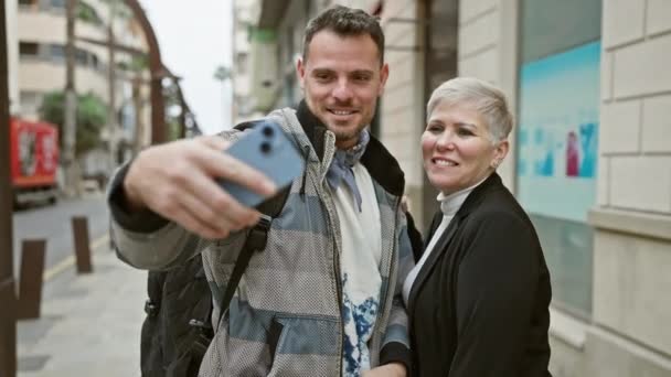 Άνδρας και γυναίκα ποζάρουν για σέλφι σε αστικό δρόμο με κτίρια στο βάθος - Πλάνα, βίντεο
