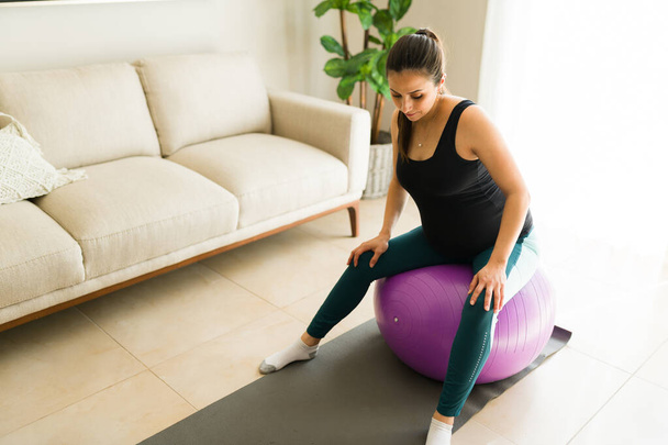 Γυμναστική έγκυος γυναίκα κάνει μια κατ 'οίκον προπόνηση χρησιμοποιώντας μια μπάλα γυμναστικής και ανύψωσης αλτήρες μένοντας υγιείς για τον τοκετό και την εγκυμοσύνη - Φωτογραφία, εικόνα