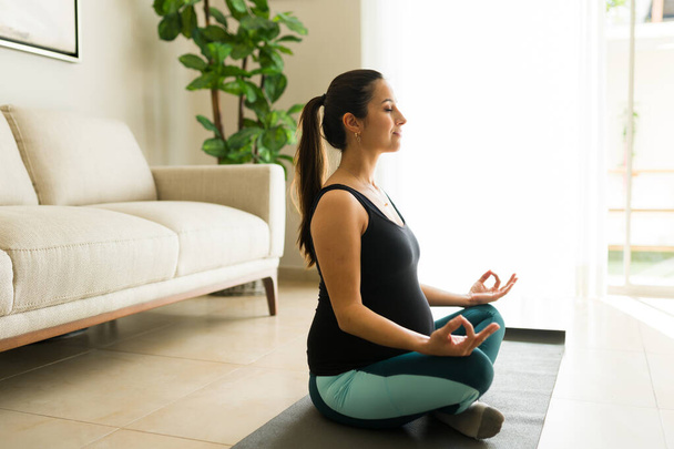 Çekici, beyaz, koca göbekli hamile kadın sağlıklı bir annelik için evde iken yoga ve nefes egzersizi yapıyor. - Fotoğraf, Görsel