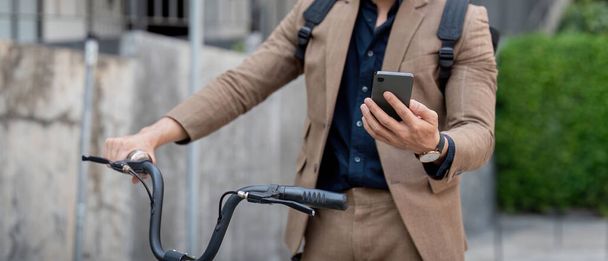 Biznesmen z rowerem za pomocą smartfona. Człowiek dojeżdżający do pracy na rowerze. Ekologiczny pojazd, koncepcja zrównoważonego stylu życia. - Zdjęcie, obraz