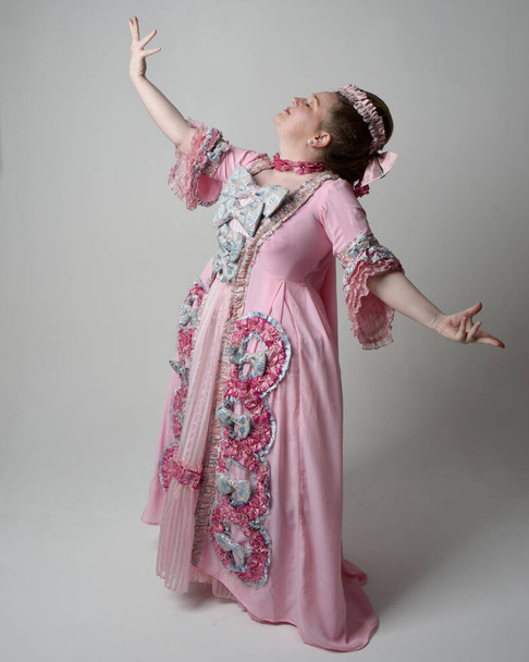 Portrait complet de femme portant une robe rose baroque française historique dans le style de Marie Antoinette avec une coiffure élégante. pose debout, danse avec les bras levés, isolé sur fond de studio. - Photo, image