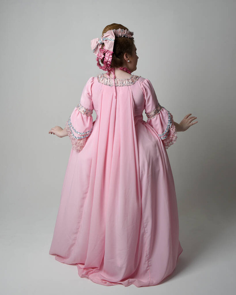 Retrato completo de mujer vestida con histórico barroco francés vestido rosa en estilo de María Antonieta con peinado elegante. Posar de pie, alejarse de la cámara, aislado en el fondo del estudio. - Foto, Imagen
