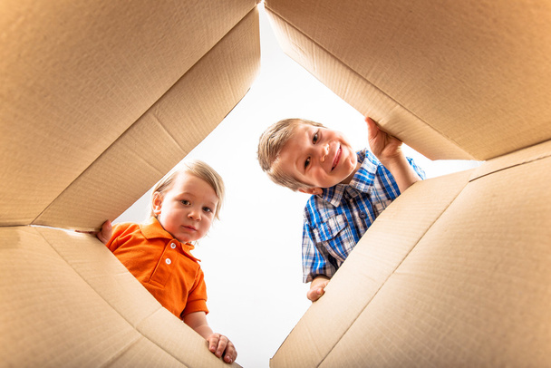 Dos niños pequeños abriendo la caja de cartón y mirando dentro con sorpresa
. - Foto, imagen