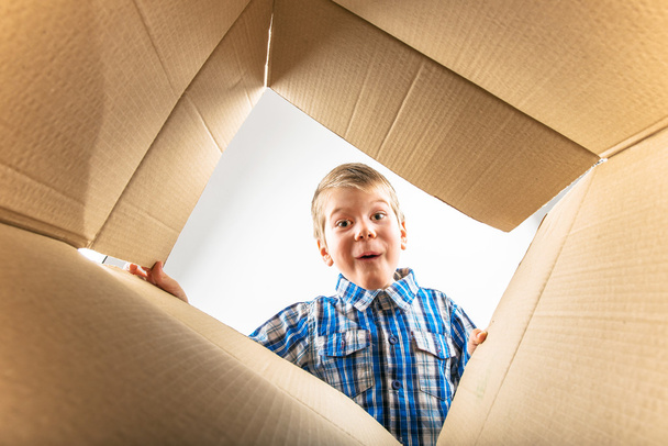 Child opening cardboard box and looking inside with surprise - Photo, Image