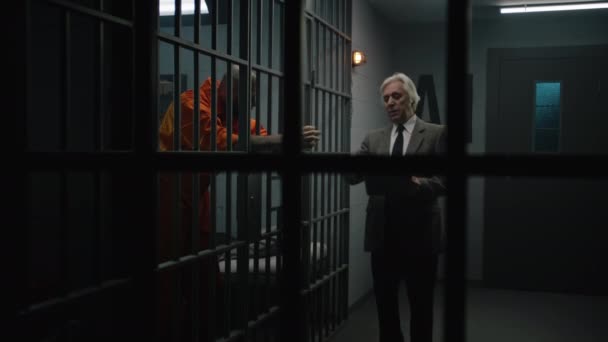 Crimineel in oranje uniform leunt op cel bars, praat met advocaat en leest advocatencontract. Gevangene zit gevangenisstraf uit voor misdaad in de gevangenis. Gangster in detentiecentrum. - Video