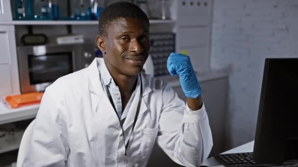Веселий афроамериканський вчений в лабораторії, одягнений в рукавички, впевнено вказуючи великий палець, відкрито посміхається з радістю. захоплююче відображення довіри та позитиву в приміщенні! - Кадри, відео