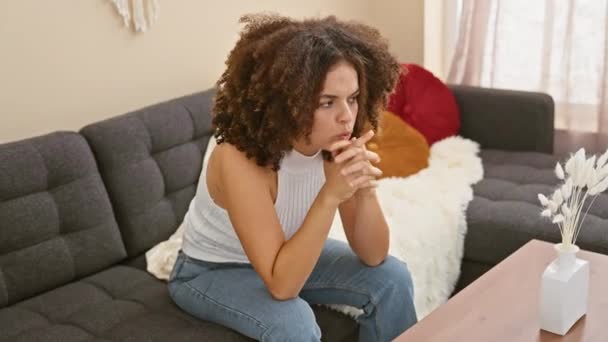 Mujer hispana nerviosa con el pelo rizado bajo estrés, uñas mordidas, mirada ansiosa en el sofá, en casa - Imágenes, Vídeo