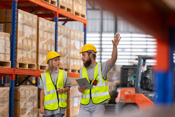 Male and Female professional worker wearing safety uniform using tablet inspect goods on shelves in warehouse. supervisor worker checklist stock inspecting product in storage for logistic. - Photo, Image