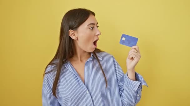 Şaşırtıcı genç İspanyol kadın, şok ve güvensizlik içinde ağzı açık, izole edilmiş sarı arka planında korku dolu bir bakışla kredi kartını kavradı.. - Video, Çekim