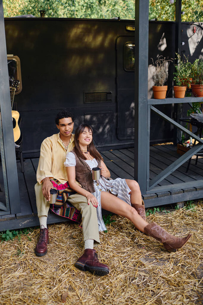 Una pareja interracial sentada cerca, disfrutando de un momento romántico en una caravana rodeada de la belleza de la naturaleza. - Foto, imagen