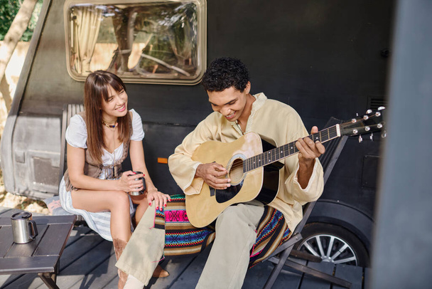 Egy férfi gitározik egy nő mellett egy romantikus környezetben, körülvéve természettel, élvezve egymás társaságát.. - Fotó, kép
