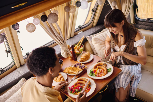 Bir çift, bir karavanın içinde sıcak bir öğle yemeğinin tadını çıkarıyor. Önlerinde lezzetli yemekler var.. - Fotoğraf, Görsel