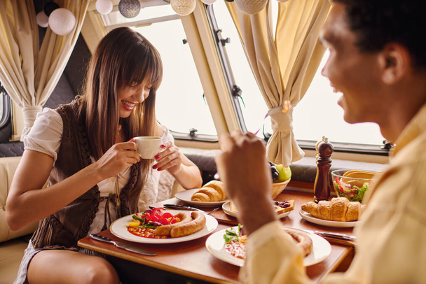Mies ja nainen istuvat ruokapöydässä nauttien romanttisesta lounaasta viihtyisässä asuntovaunussa.. - Valokuva, kuva