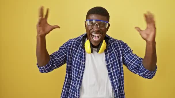Vzrušený afroameričan s bezpečnostními brýlemi, se vztyčenými pažemi v šíleném, šíleném vítězství. slaví své vítězství s radostí nad izolovaným žlutým pozadím. - Záběry, video
