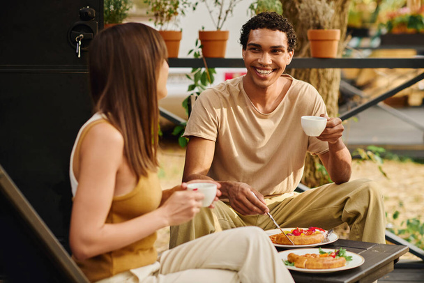 Un couple interracial dégustant un repas ensemble sur un banc, savourant leur nourriture dans un cadre confortable et intime. - Photo, image
