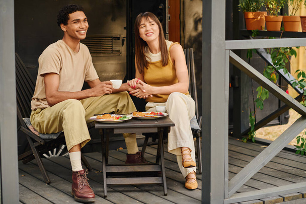 Un hombre y una mujer de diferentes razas están sentados pacíficamente en un porche, disfrutando de la compañía de los demás en un entorno tranquilo. - Foto, imagen