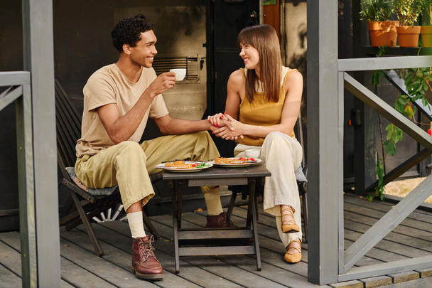 Un hombre y una mujer se sientan en un porche, disfrutando de una deliciosa comida juntos. - Foto, Imagen