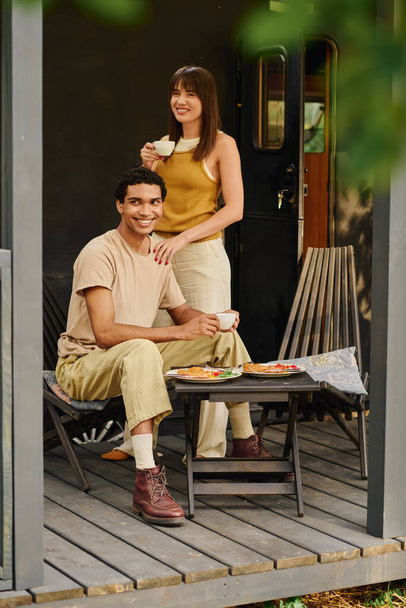 Ein gemischtrassiges Paar sitzt zusammen auf einer Veranda und genießt einen friedlichen Moment in der Gesellschaft des jeweils anderen. - Foto, Bild
