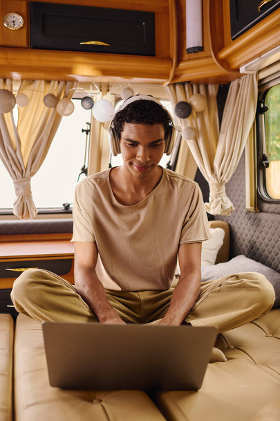 Een man van gemengde ras zitten comfortabel op een bank, gericht op zijn laptop scherm. - Foto, afbeelding