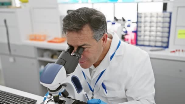 Científico masculino maduro analizando muestras a través de un microscopio en un laboratorio moderno. - Metraje, vídeo