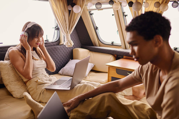 Un homme est assis à côté d'une femme sur un ordinateur portable sur un canapé confortable, tous deux profondément absorbés dans leur travail. - Photo, image