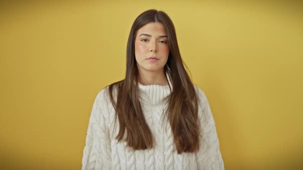 Selbstverständliches Porträt einer jungen, schönen hispanischen Frau, die selbstbewusst einen Pullover trägt und vor gelbem Hintergrund ernst in die Kamera blickt.. - Filmmaterial, Video