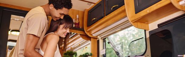 An interracial couple sitting side by side, engrossed in cooking inside of van - Photo, Image