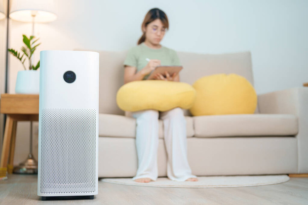 Air Purifier with woman relax and use tablet on sofa. Purification system for filter and cleaning dust PM2.5 HEPA and virus in home. Allergy, Pure air, health, Wellness lifestyle and Air Pollution - Photo, Image
