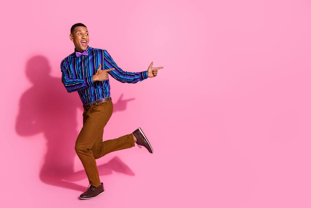 Full length photo of excited funky guy dressed striped shirt pointing two fingers empty space isolated pink color background. - Zdjęcie, obraz