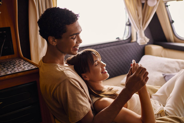 Een interraciale man en vrouw die vredig samen op een bed liggen in een gezellige setting, genietend van een romantisch moment tijdens hun uitje. - Foto, afbeelding
