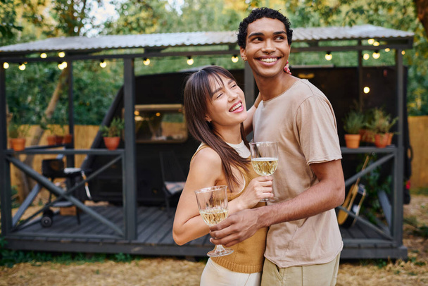 Ένας άντρας και μια γυναίκα τσουγκρίζουν ποτήρια κρασιού, απολαμβάνοντας μια ρομαντική στιγμή σε ένα άνετο τροχόσπιτο. - Φωτογραφία, εικόνα