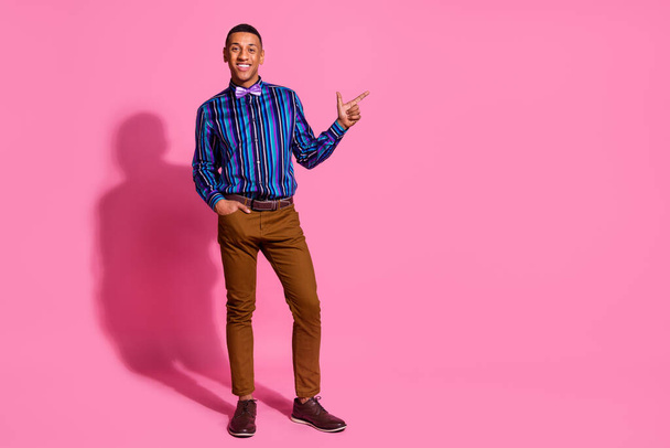 Full length photo of positive funky guy wear striped shirt showing finger empty space isolated pink color background. - Φωτογραφία, εικόνα