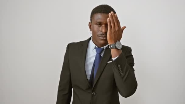 Mosolygó magabiztos afro-amerikai férfi játékosan befedi az egyik szemét kézzel, miközben áll egy elegáns öltöny ellen elszigetelt fehér háttér - Felvétel, videó
