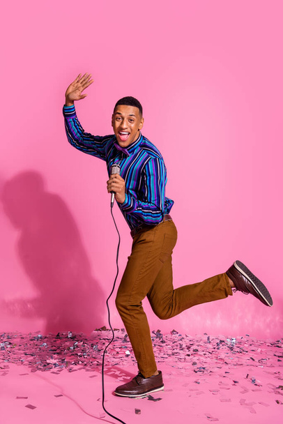 Full length vertical photo of cheerful excited guy wear striped shirt dancing singing microphone isolated pink color background. - Foto, imagen