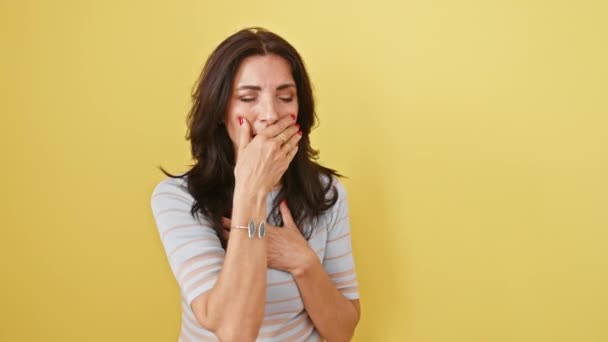 Unwell mature hispanic woman, coughing from cold or bronchitis, alone on yellow background hinting at health care needed - Footage, Video