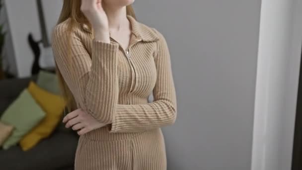 Mujer rubia joven confiada usando suéter relajante en casa, pose de perfil con sonrisa natural mirando hacia los lados - Imágenes, Vídeo
