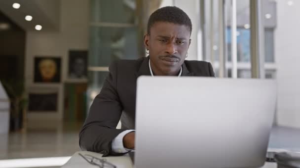 Hombre africano enfocado que trabaja en la computadora portátil en la oficina moderna, mostrando profesionalidad y concentración. - Imágenes, Vídeo
