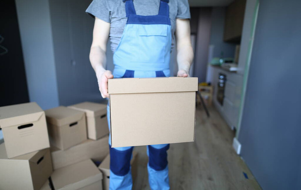 Close-up of worker hands holding empty cardboard box. Professional carpenter or foreman. Room full with cartons. Interior designer and renovation in new apartment concept - Photo, Image