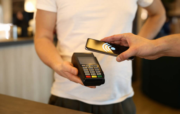 Close-up of customer person making payment via terminal and mobile phone in cafe. Pay by smartphone. Contactless nfc and modern device technology concept - Photo, Image