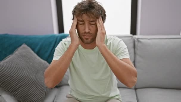 Stres hispánec s vousy sedí uvnitř na pohovce drží hlavu v dlaních projevující úzkost. - Záběry, video