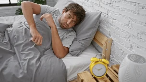 Een vermoeide man ligt in bed, ogen dicht, met een prominente wekker in zijn minimalistische slaapkamersetting. - Video
